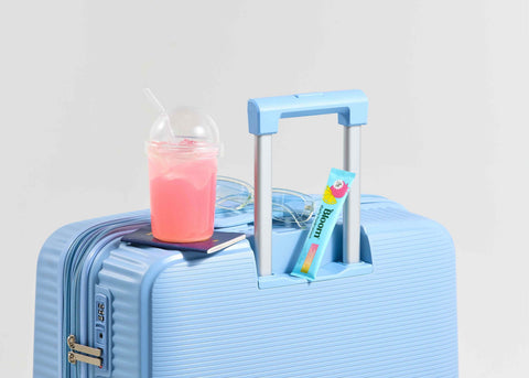 Blue suitcase with a pink drink and a book on a light gray background
