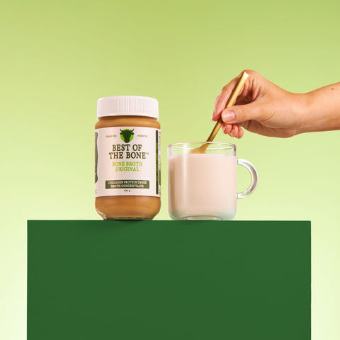 Person stirring a glass of milk with a jar of 'Best of the Bone' product on a green background